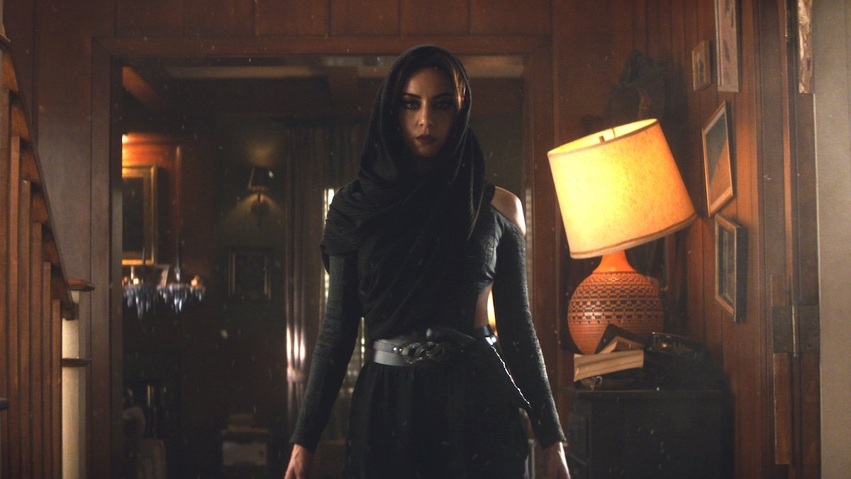 Aubrey Plaza in black with a black hood in a house on Agatha All Along